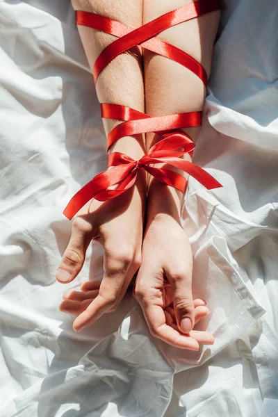 Cropped shot of male and female hands tied with red ribbon on bed — Stock Photo