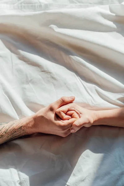 Partial view of couple in live holding hads while lying in bed together — Stock Photo