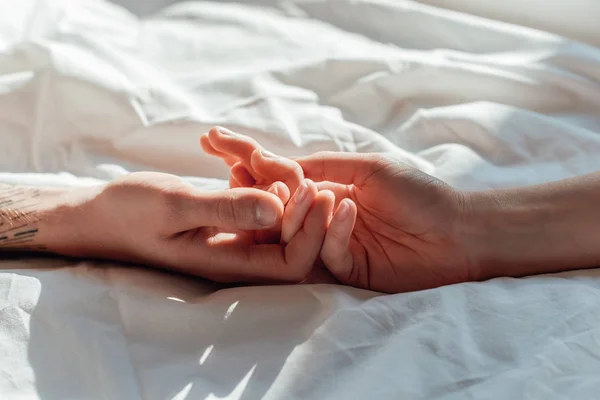 Partial view of couple in live holding hads while lying in bed together — Stock Photo