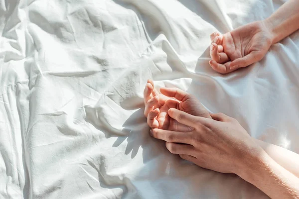 Partial view of couple in live holding hads while lying in bed together — Stock Photo