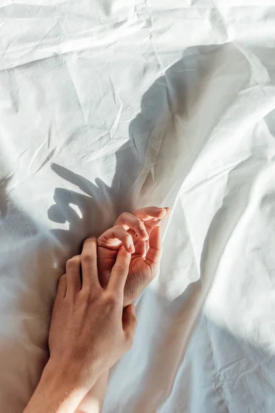 Partial view of couple in live holding hads while lying in bed together — Stock Photo