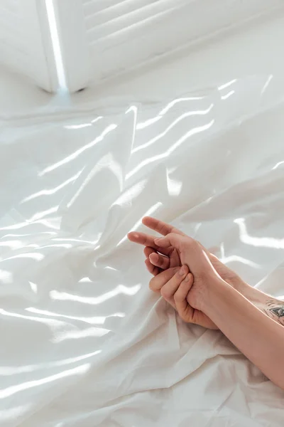 Partial view of loving couple holding hands while lying on white bed sheet — Stock Photo