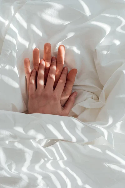 Partial view of loving couple holding hands while lying under blanket together — Stock Photo