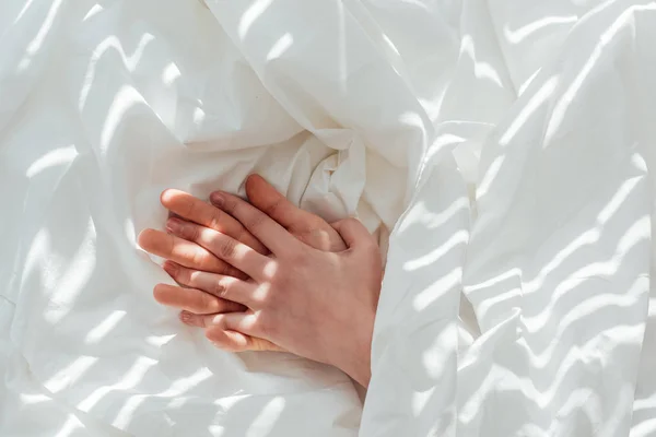 Partial view of loving couple holding hands while lying under blanket together — Stock Photo