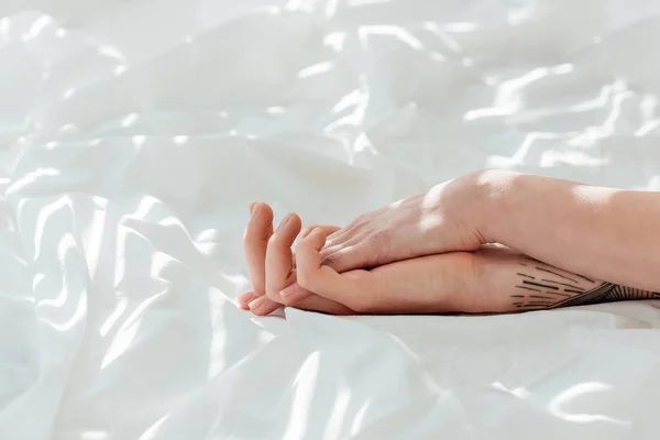 Частковий вид люблячої пари, що тримає руки, лежачи на білому простирадлі — стокове фото