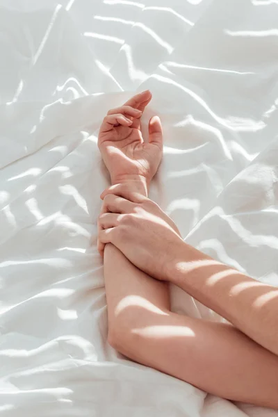 Cropped shot of loving couple lying on white bed sheet together — Stock Photo