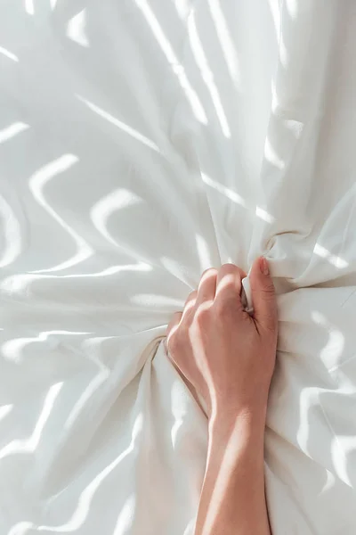 Vue partielle de la femme tenant un drap de lit blanc alors qu'elle était couchée au lit — Photo de stock