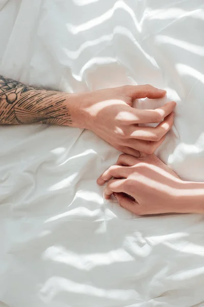 Cropped shot of loving couple lying on white bed sheet together — Stock Photo