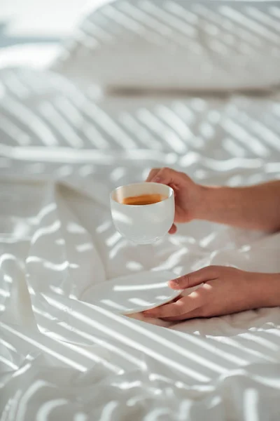 Teilbild einer Frau mit einer Tasse Kaffee im Bett am Morgen — Stockfoto