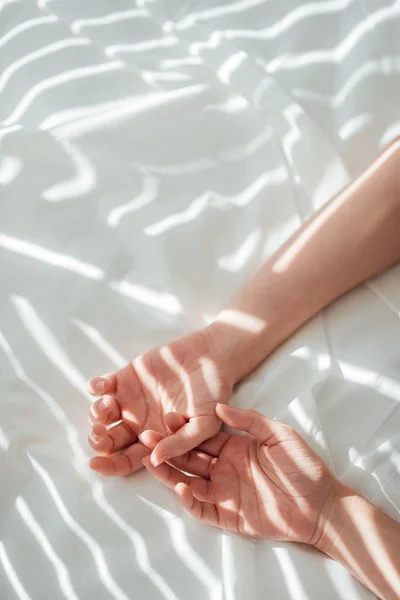 Recortado tiro de las manos femeninas en la hoja de cama blanca - foto de stock