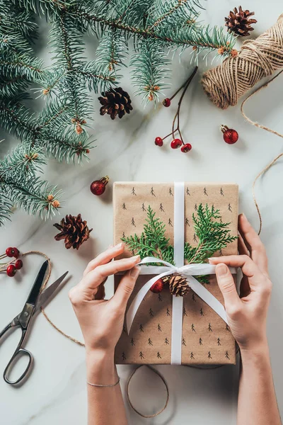 Vista recortada de la mujer decorando regalo de Navidad con cinta y ramas de abeto - foto de stock