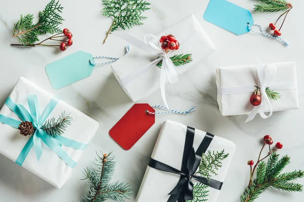 Pose plate avec cadeaux de Noël, branches de sapin, baies décoratives et étiquettes sur fond de marbre — Photo de stock