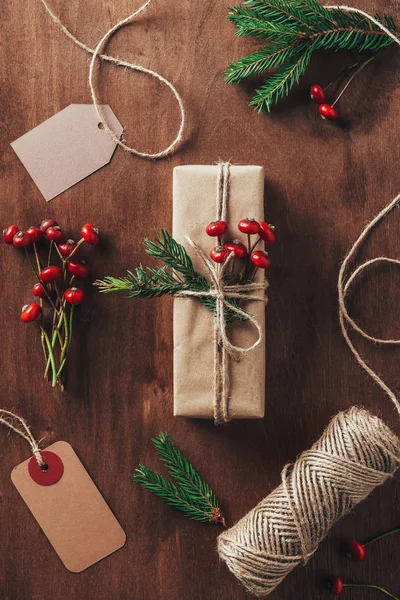 Плоский лежал с рождественским подарком ели ветви, декоративные ягоды, бечевка и бирки на деревянном фоне — стоковое фото
