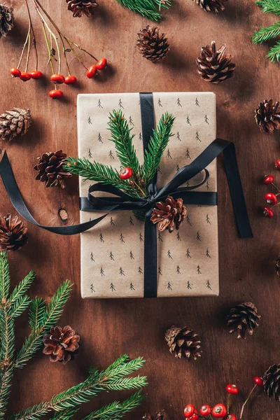 Vista dall'alto del regalo di Natale con rami di abete, pigne e bacche decorative su sfondo di legno — Foto stock