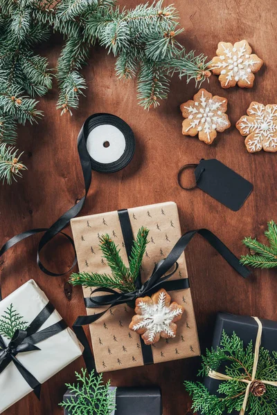 Acostado plano con cajas de regalo de Navidad, cintas, ramas de abeto y galletas de copo de nieve sobre fondo de madera - foto de stock