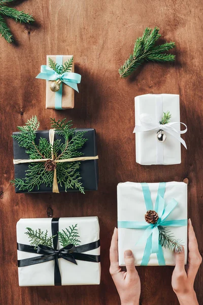 Abgeschnittene Ansicht einer Frau, die Weihnachtsgeschenke mit Tannenzweigen auf Holzgrund hält — Stockfoto