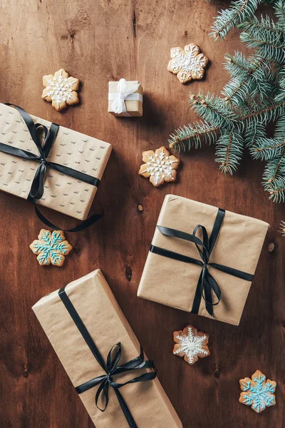 Acostado plano con cajas de regalo de Navidad, rama de abeto y galletas sobre fondo de madera - foto de stock