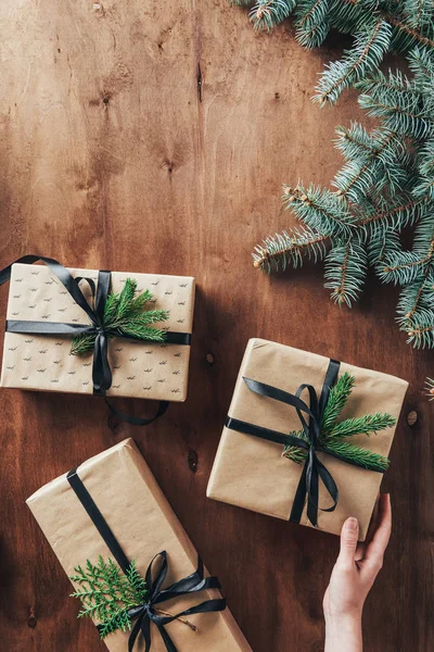 Cropped view of woman touching gift boxes on wooden background with christmas tree branches — Stock Photo