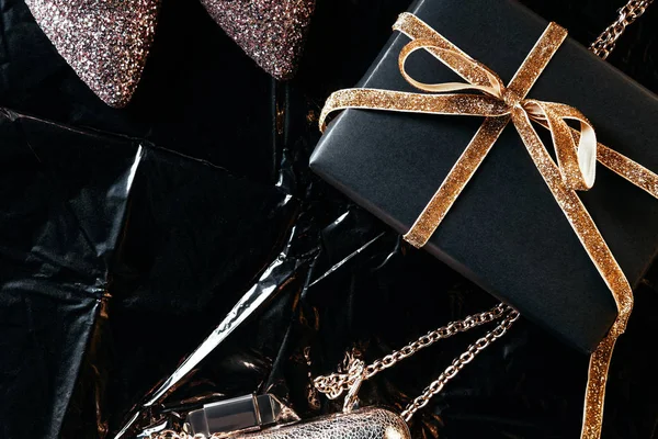 Vista dall'alto della disposizione con regalo avvolto, scarpe femminili e borsa su sfondo di carta da imballaggio nero — Foto stock