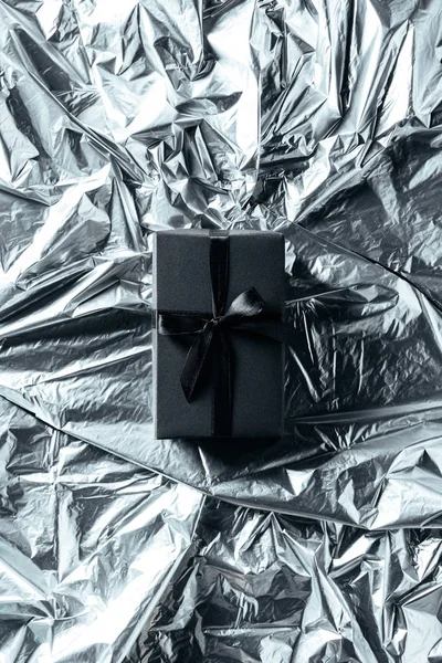 Vista superior da caixa de presente com fita preta no fundo de papel de embrulho prateado — Fotografia de Stock