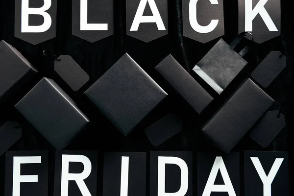 Top view of black friday lettering, blank price tags, shopping bag and boxes on black background — Stock Photo