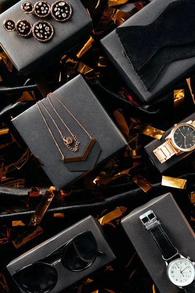 Plat couché avec des chaussures féminines, sac à main et bijoux sur fond noir avec confettis dorés — Photo de stock