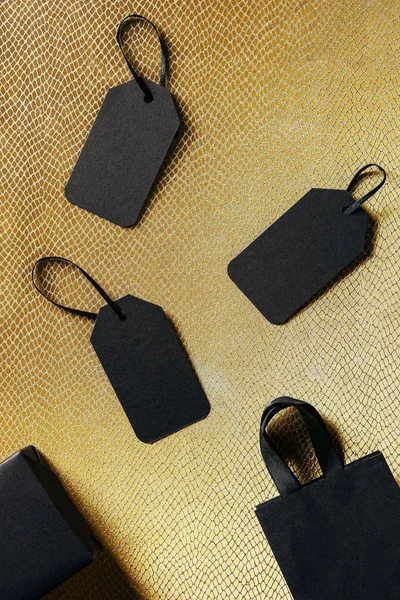 Верхний вид черных пустых ценников, коробка и сумка для покупок на золотом фоне, черная пятница концепции — стоковое фото