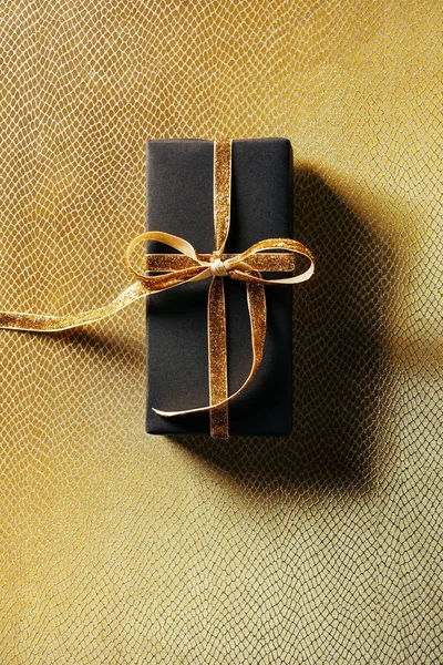 Top view of wrapped gift box with golden ribbon on golden background — Stock Photo