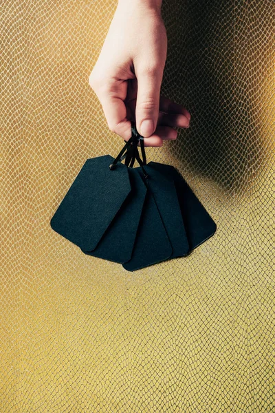 Cropped shot of man holding black blank price tags on golden backdrop, black friday concept — Stock Photo