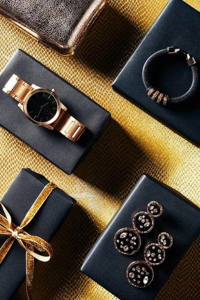 Flat lay with wrapped gift, feminine jewelry and purse on golden backdrop — Stock Photo