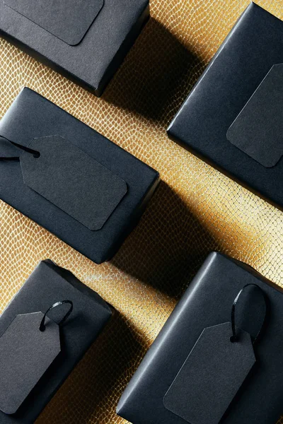 Pose plate avec des boîtes noires avec des étiquettes de prix vierges sur fond doré, concept de vendredi noir — Photo de stock