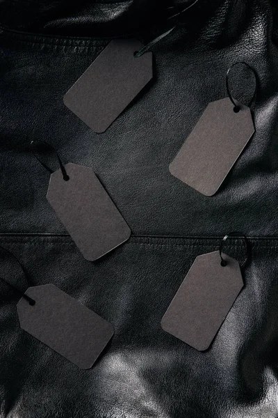 Top view of arranged blank price tags on black leather jacket background, black friday concept — Stock Photo