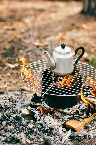 Metallic kettle on grill over fireplace on autumnal background — Stock Photo