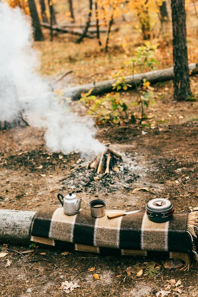 Camping kitchenware and smoking fireplace in autumn forest — Stock Photo