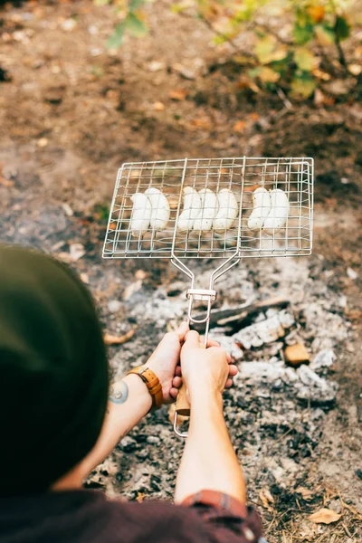 Hands of man roasting row of sausages on grill grate over fire in autumn — Stock Photo