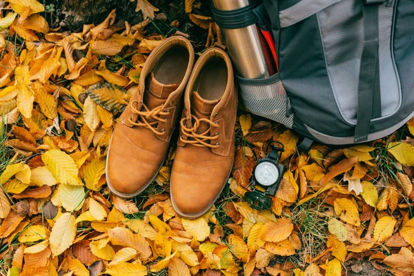 Vista superior de los suministros de camping y botas de color naranja en hermoso follaje de otoño - foto de stock