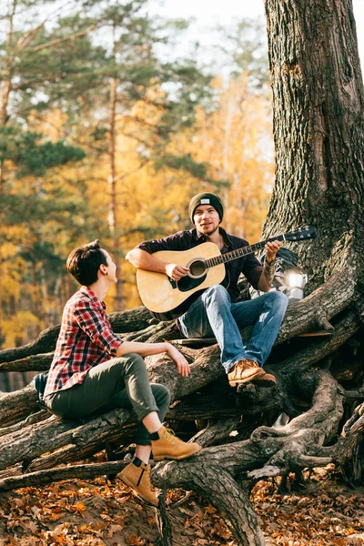 Happy woman and man having fun with guitar on autumal background — Stock Photo