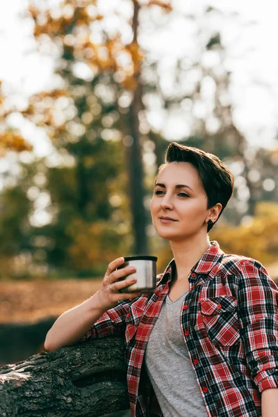 Adult woman holding metallic thermos cup on blurred autumnal background — Stock Photo