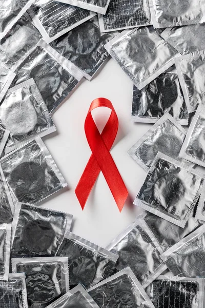 Draufsicht auf Hilfsmittel Bewusstsein rotes Band und silberne Kondome auf weißem Hintergrund — Stockfoto