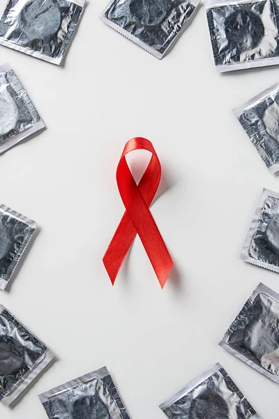 Vista superior da conscientização ajudas fita vermelha e preservativos de prata no fundo branco — Fotografia de Stock