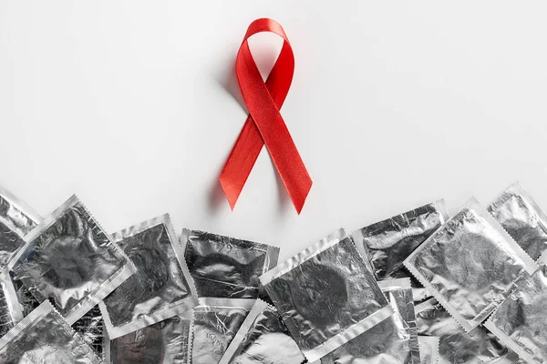 Vue du dessus du ruban rouge de sensibilisation au sida et des préservatifs en argent sur fond blanc, concept médical — Photo de stock
