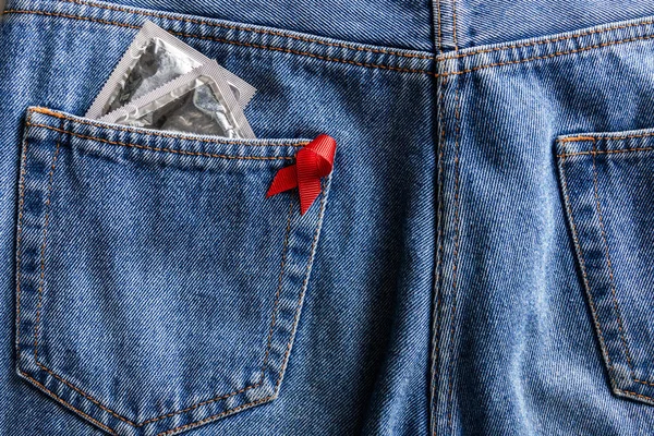 Aide à la sensibilisation ruban rouge et préservatifs en argent dans la poche de jeans bleus — Photo de stock