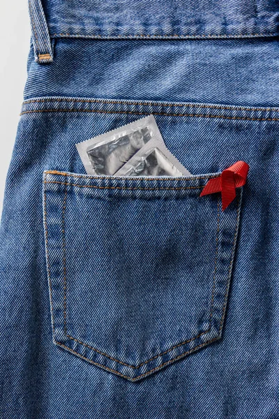 Aids awareness red ribbon and silver condoms in pocket of blue jeans — Stock Photo