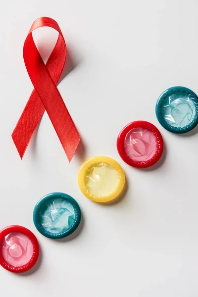 Vista superior de la cinta roja de sensibilización de sida y condones multicolores sobre fondo blanco - foto de stock