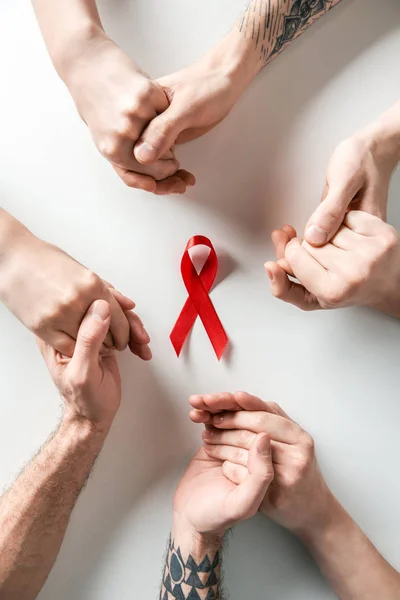 Top view of people holding hands and aids awareness red ribbon on white background — Stock Photo