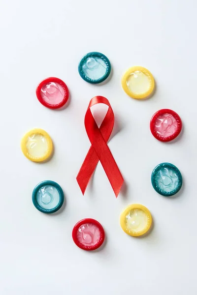 Vista superior de la cinta roja de sensibilización de sida y condones multicolores sobre fondo blanco - foto de stock