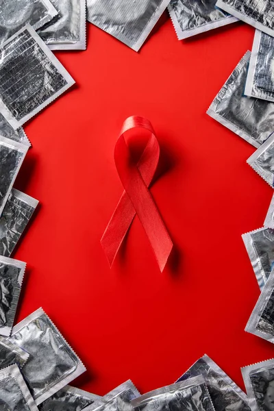Draufsicht auf Hilfsmittel Bewusstsein rotes Band und silberne Kondome auf rotem Hintergrund — Stockfoto