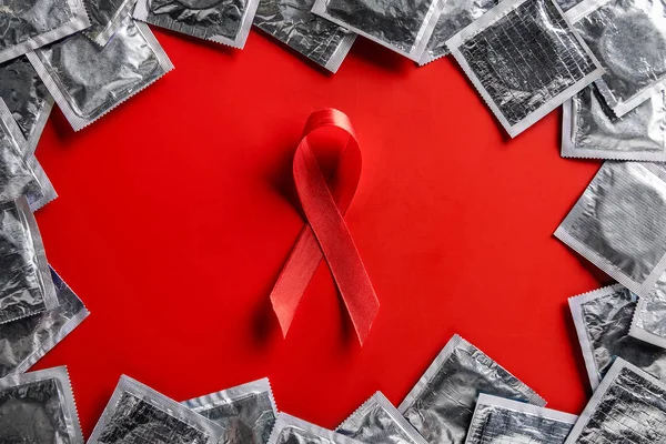 Top view of aids awareness red ribbon and silver condoms on red background — Stock Photo