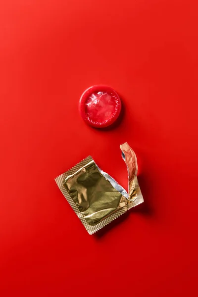 Top view of red condom and golden packaging on red background — Stock Photo