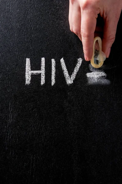 Vista superior de la mano femenina que sostiene el condón con el cartel del hiv en el fondo negro - foto de stock